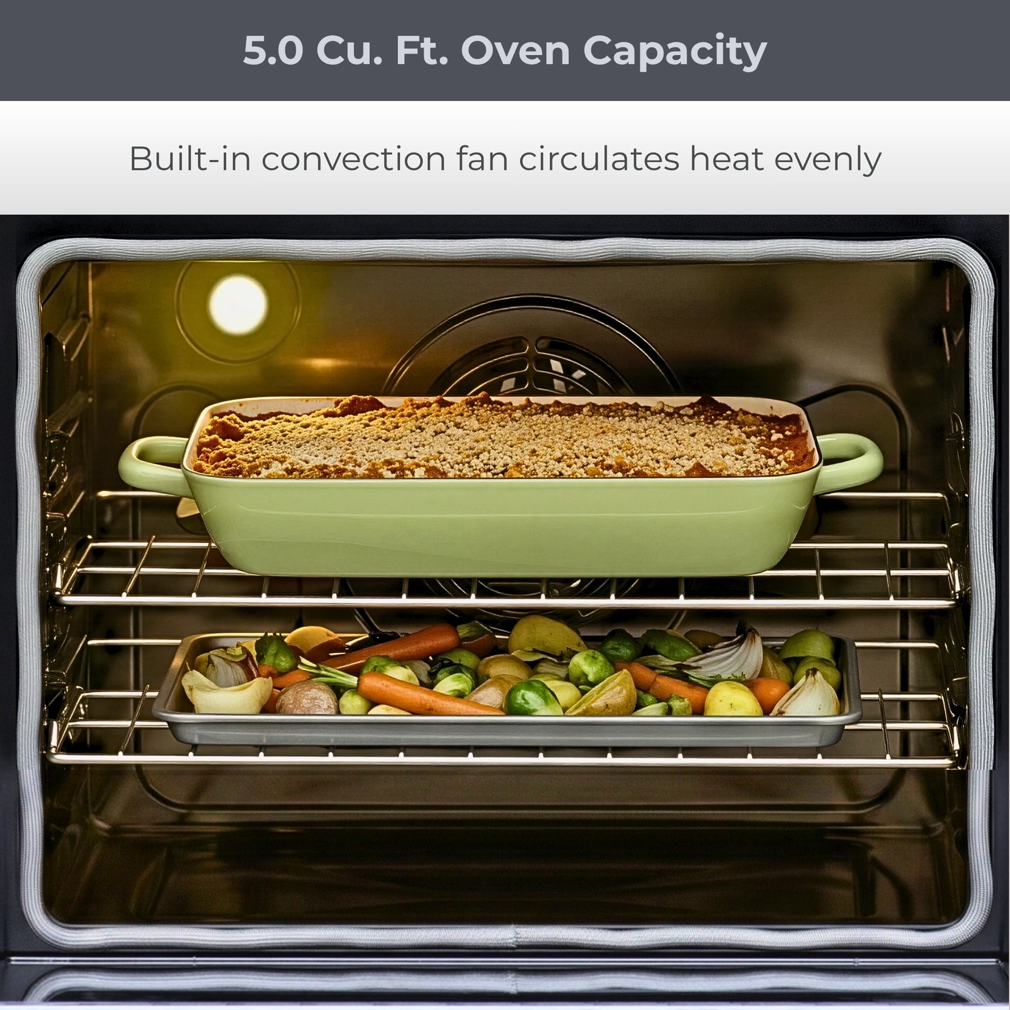 Closeup of the open Kenmore stainless steel electric range showing food cooking on two racks. Text above reads, "5.0 Cu. Ft. Oven Capacity: Built-in convection fan circulates heat evenly"